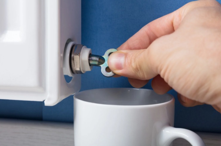 persona che sfiata un termosifone con accanto una tazza