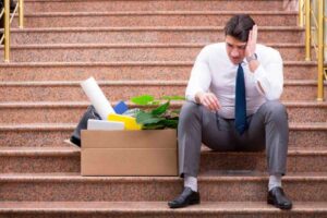 uomo triste seduto sulle scale con accanto uno scatolone