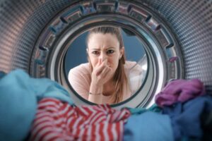 donna che si tappa il naso davanti al cestello della lavatrice