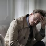 uomo preoccupato seduto sul divano con una mano sulla fronte